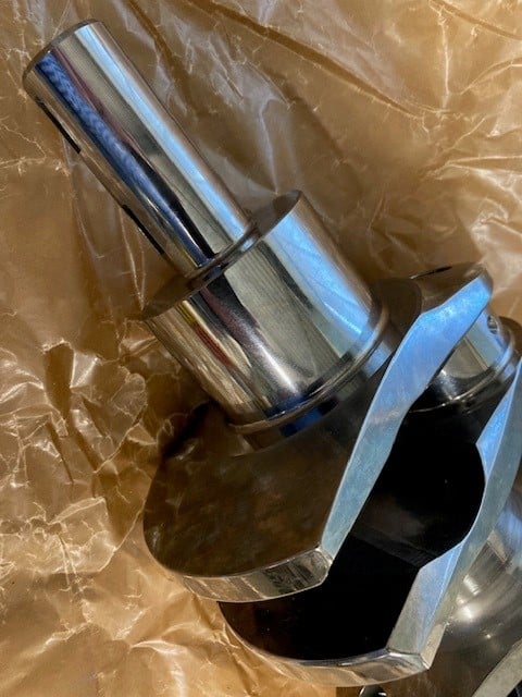 A detailed close-up photo of the Arrow Precision Engineering Billet Steel Crankshaft, Narrow Journal – TR2-4, Morgan +4, displays its lustrous, finely machined cylindrical surfaces and precise edges as it rests on crumpled brown paper—perfectly crafted for classic models like the Morgan +4 and TR2-4.