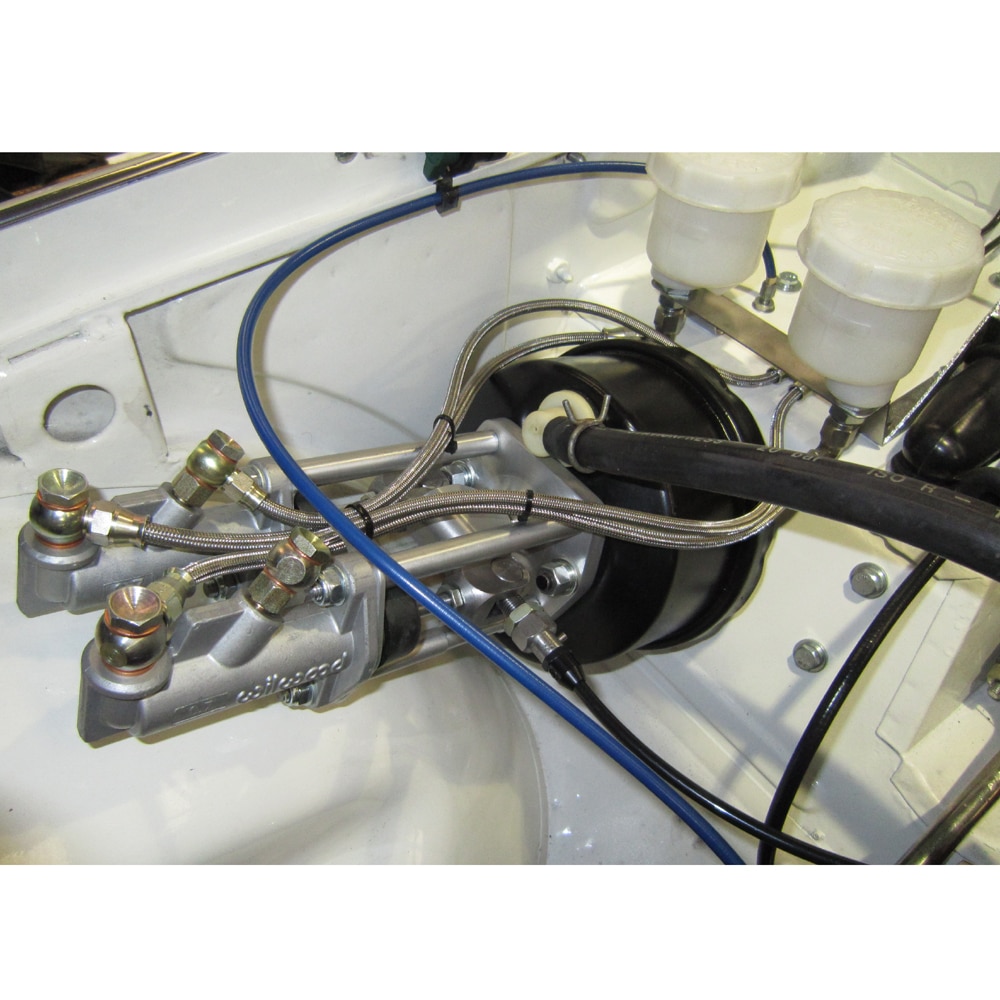 Detailed view of a car's brake system with metallic brake lines, fittings, and a Racetorations Dual Brake Bias Master Cylinder Assembly - TR5-6 visible, set against a white background.