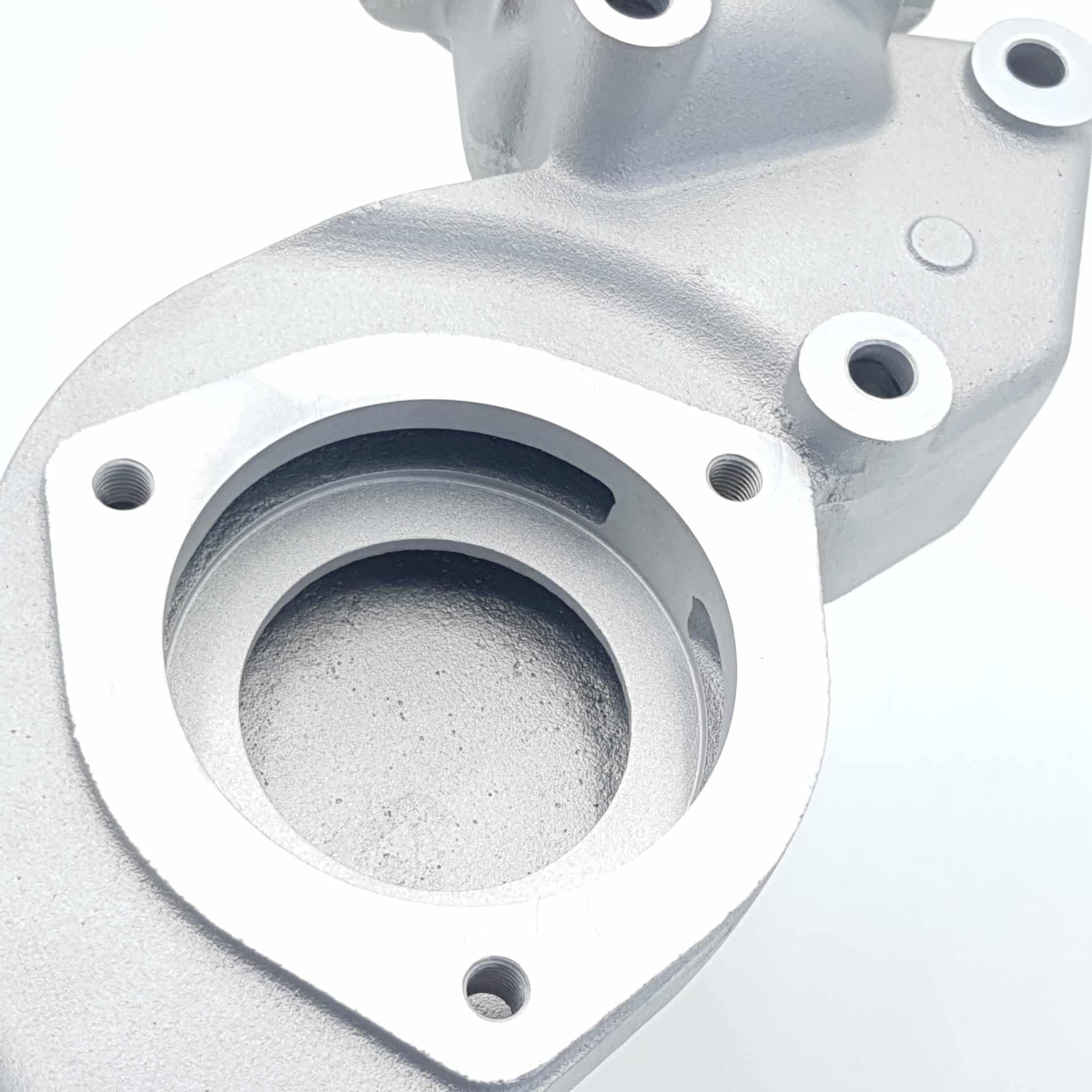 A close-up of the Racetorations Aluminium Water Pump Housing for Triumph TR5, TR250 & TR6, featuring a textured metallic finish, multiple circular openings, and bolt holes, displayed against a white background.