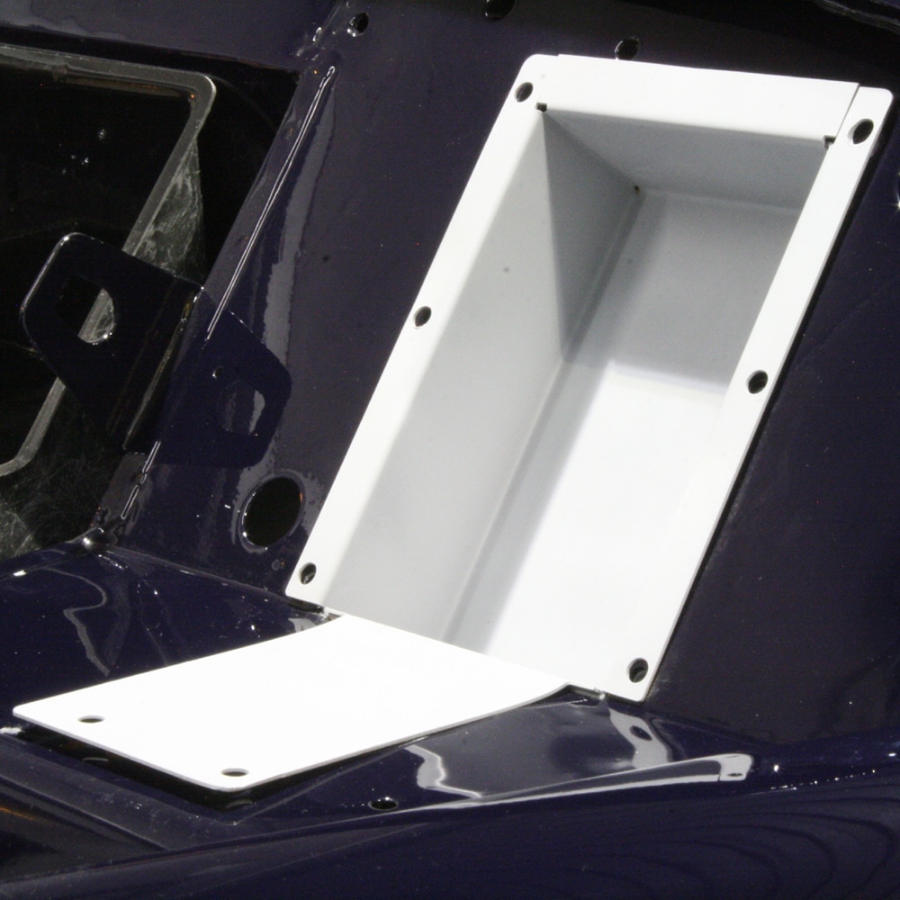 A close-up of a rectangular, white Racetorations Hidden Fuse & Relay Box - TR2-3A with a hinged lid, mounted on a dark surface. The open lid reveals the empty compartment inside, highlighting its recessed and concealed design.