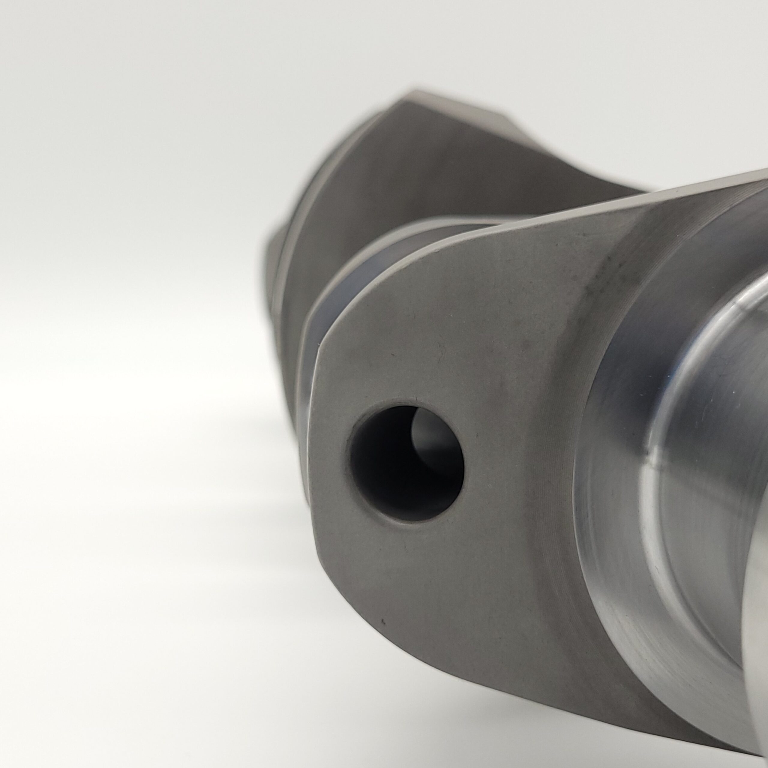 Close-up of an Arrow Precision Engineering Billet Steel Crankshaft, Standard Journal – TR2-4, Morgan +4, showing its smooth machined surfaces and circular hole against a white background, emphasising the edges and curved form of the part.