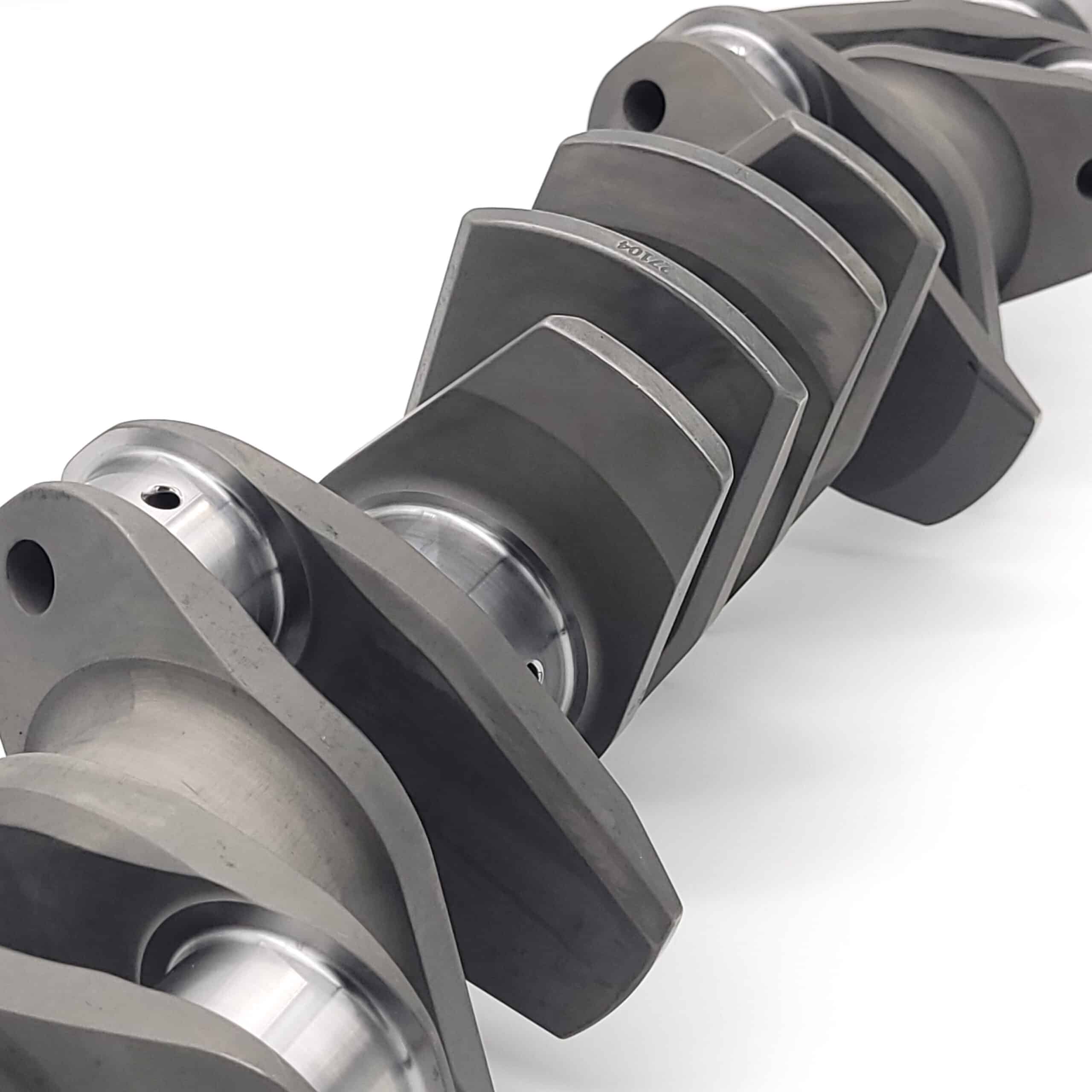 Close-up of an Arrow Precision Engineering Billet Steel Race Crankshaft for TR5-6, showing its machined surfaces and lobed geometry against a plain white background.