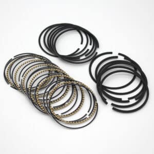 A collection of metallic piston rings, some with a gold-coloured textured surface, arranged in neat overlapping rows and separate stacks on a white background.