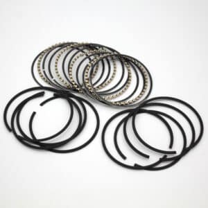 A set of black piston rings and metal oil control rings arranged on a white surface, used in engine components for sealing and regulating oil consumption.