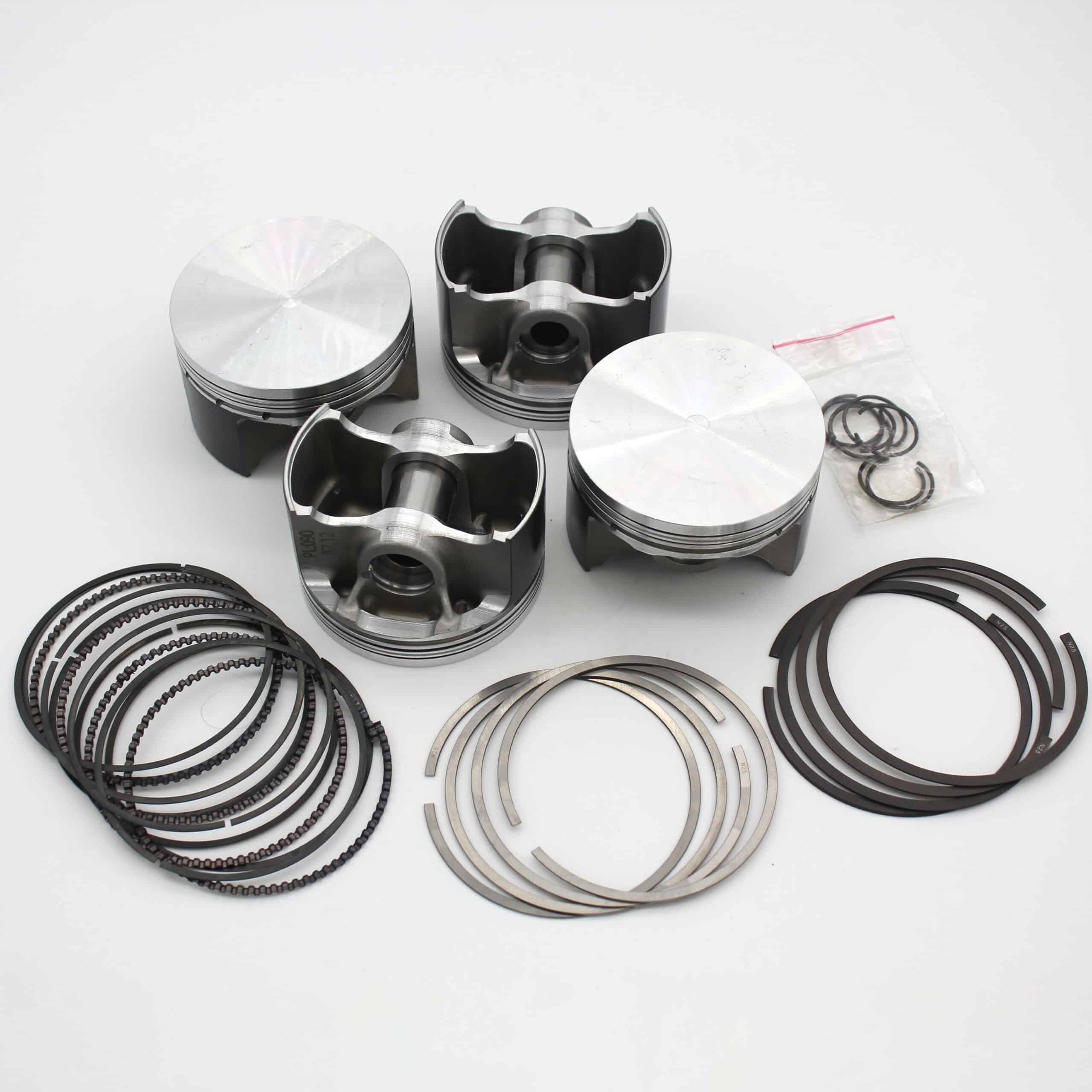 Four metal engine pistons are arranged on a white surface, accompanied by piston rings, circlips, and other small engine components organised in separate groups.