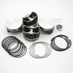 Four metallic engine pistons are arranged upright and on their sides, surrounded by various piston rings and a small plastic bag with additional rings, all set against a plain white background.