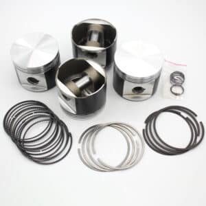 Four metallic engine pistons with connecting rods are arranged on a white surface, along with several sets of piston rings and a small plastic bag containing additional rings or clips.