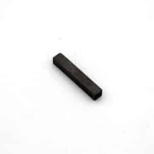 A small, rectangular, dark-coloured metal bar lies on a plain white surface.