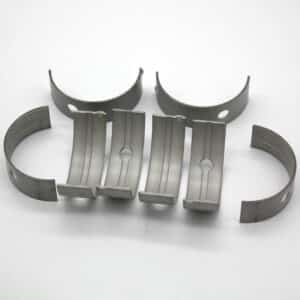 Six metal engine bearings are arranged in two rows on a white background; the top row shows three bearings upright, while the bottom row displays three bearings with inner surfaces and lubrication holes visible.