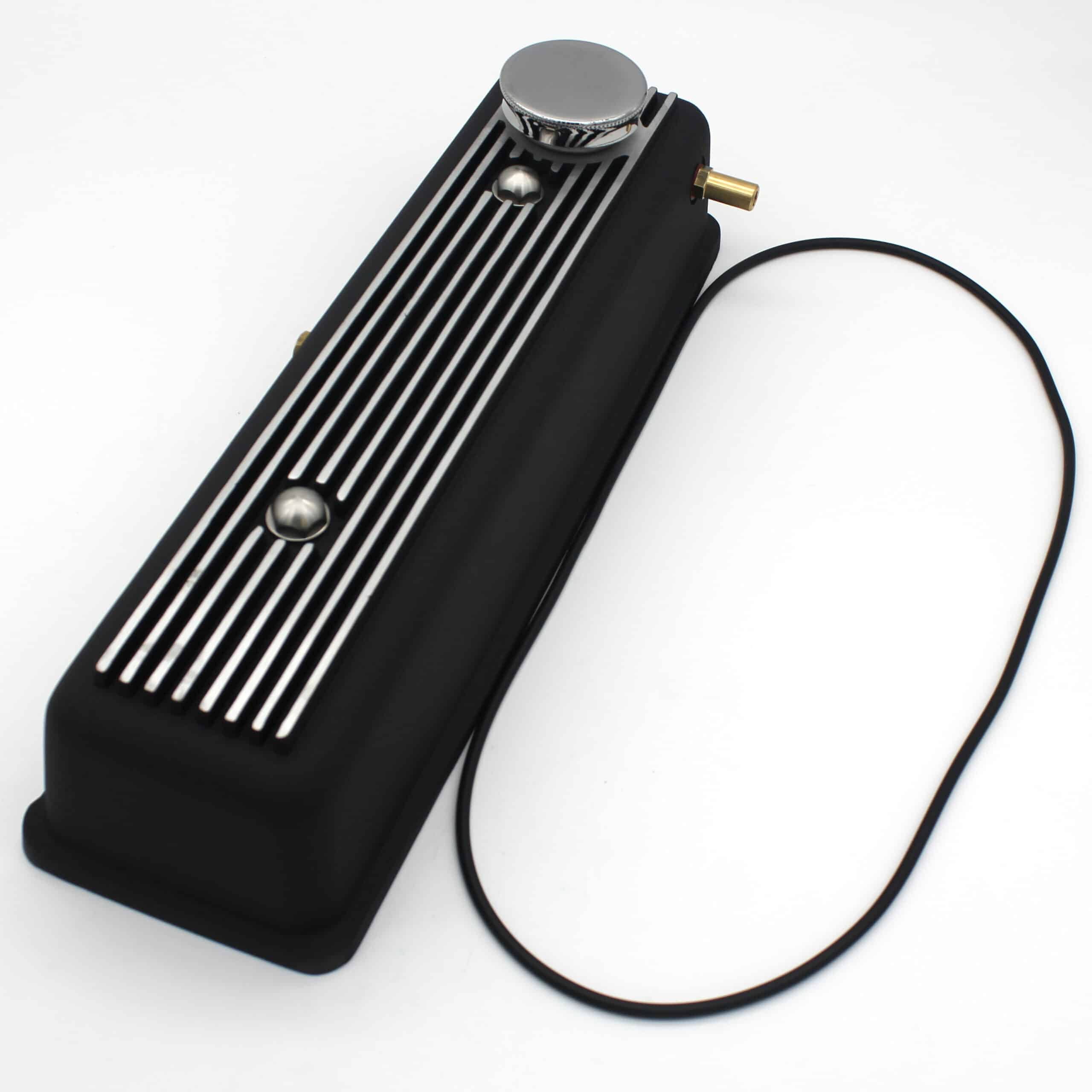 A black engine valve cover with silver horizontal stripes, a round chrome oil cap, and a thin black rubber gasket lying beside it on a white background.