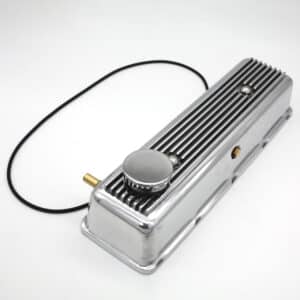 A shiny silver metal valve cover with vents, a round cap, a black rubber hose attached, and a small brass fitting, all placed on a white background.