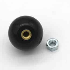 A black spherical knob with a brass threaded insert sits next to a silver hex nut on a white surface.