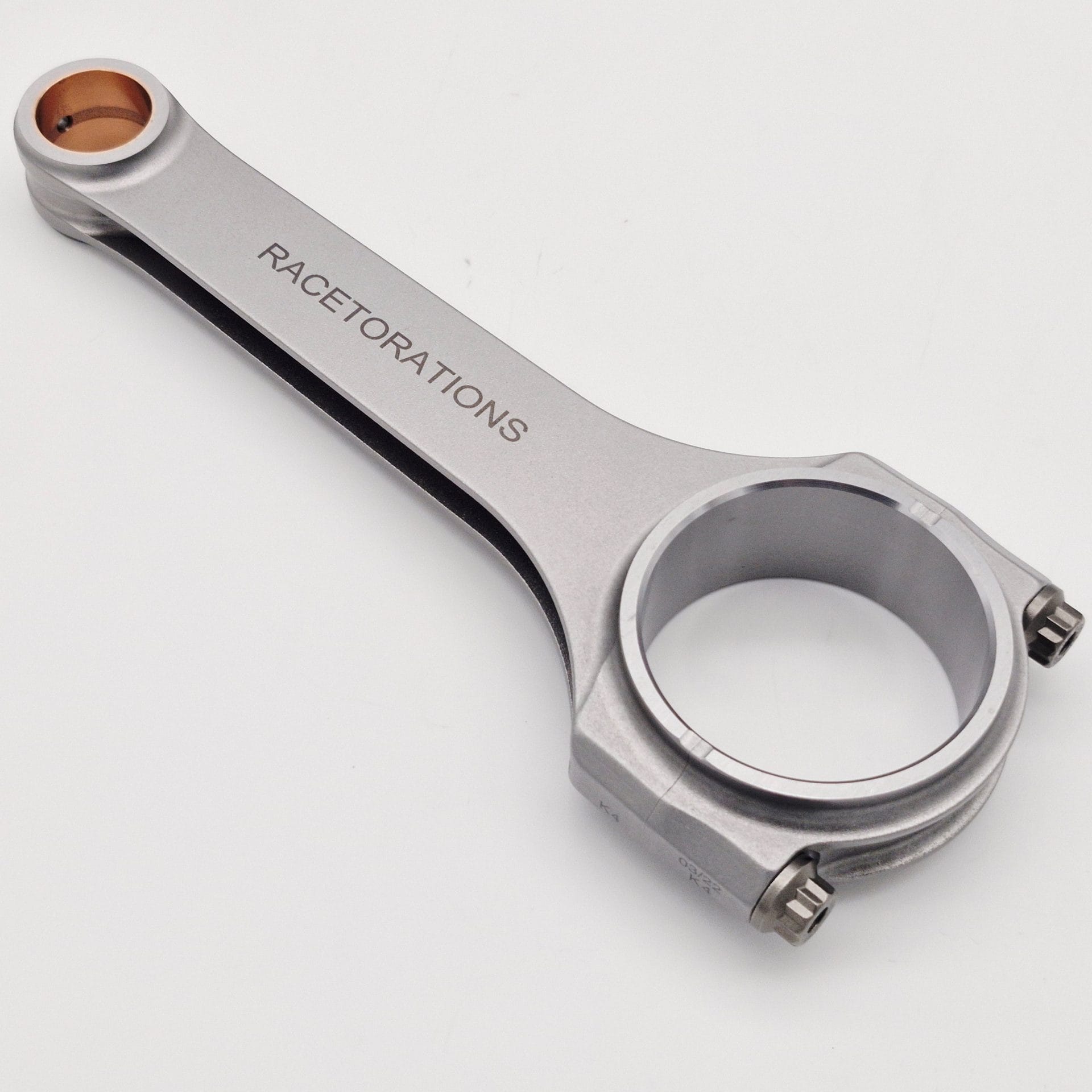 A Racetorations 87mm Slipper Piston & Steel Connecting Rod rests on a white surface, showing a bronze bushing and two bolts—designed for TR2-4A & Morgan +4 engines.