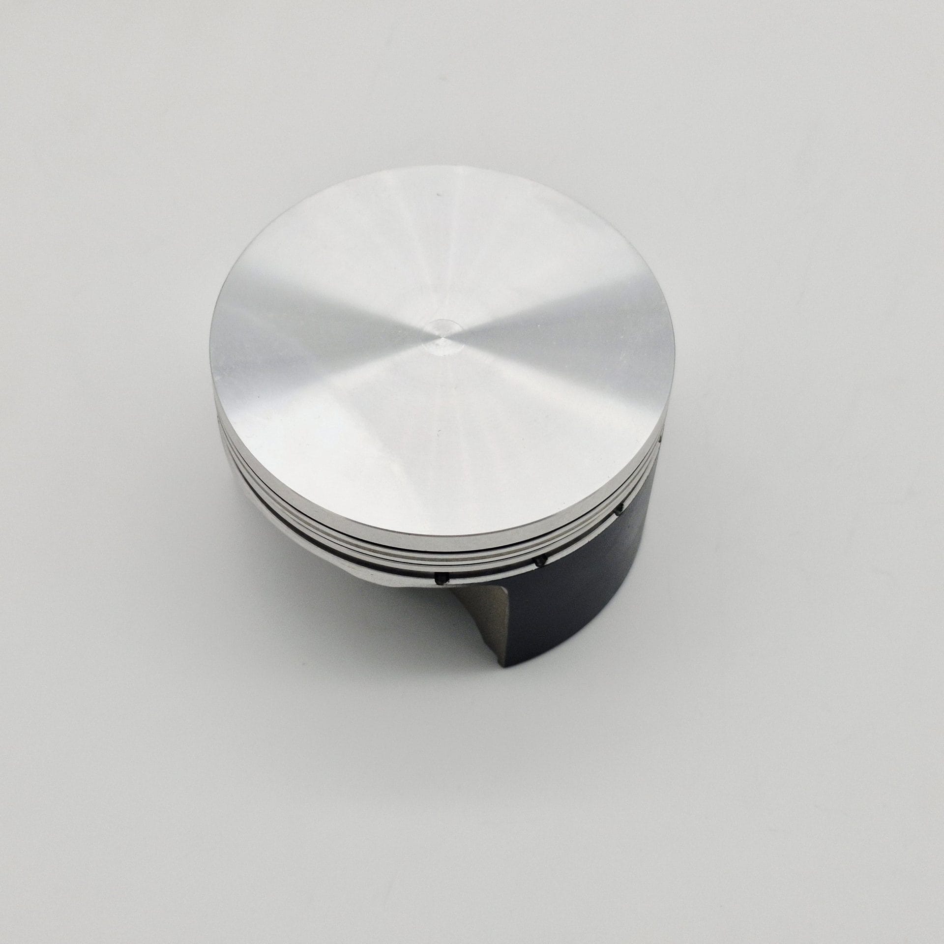 A Racetorations 87mm Slipper Piston & Steel Connecting Rod for TR2-4A & Morgan +4, featuring thin grooves and a shiny silver finish, rests on a plain white background, viewed from above at an angle.