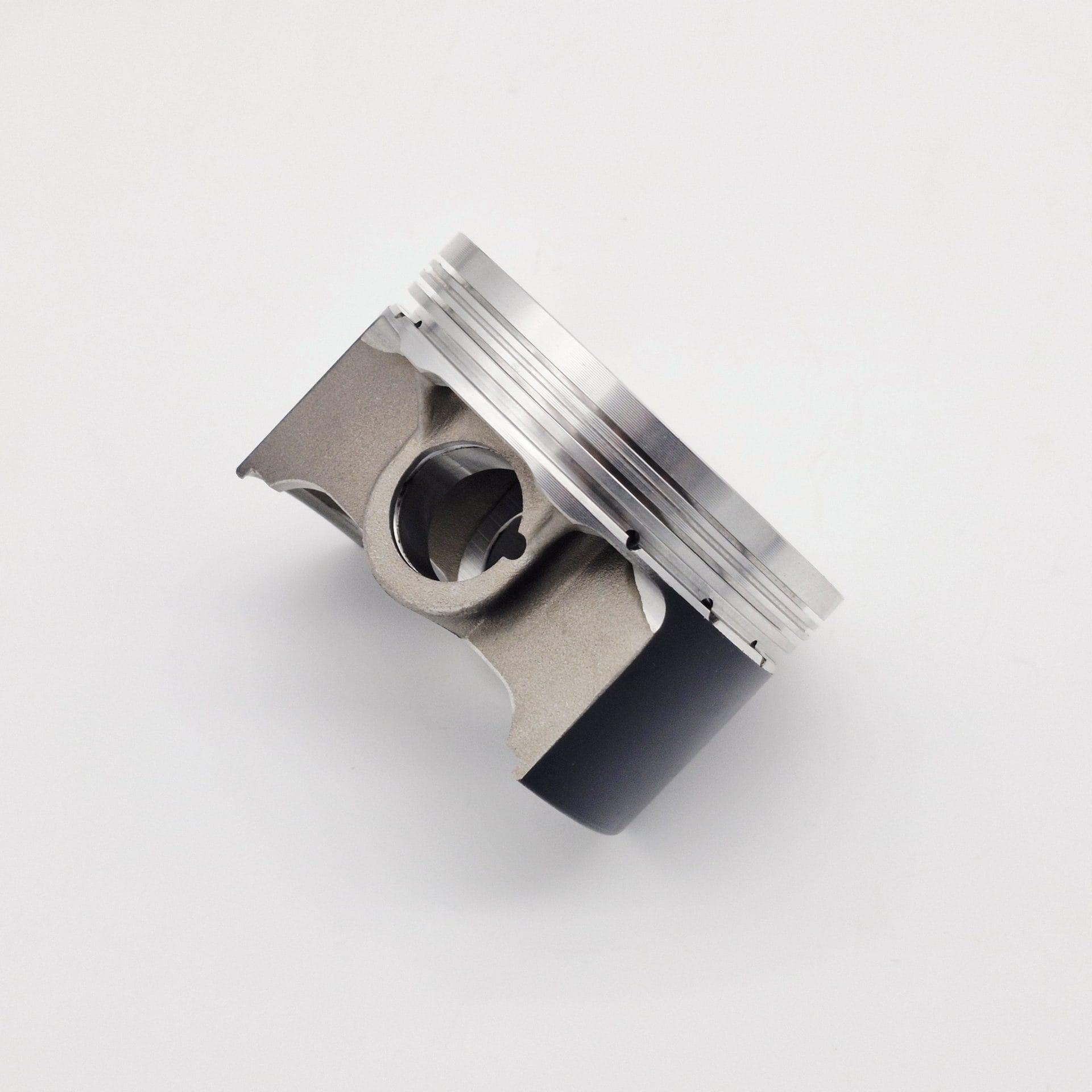 An 87mm Racetorations slipper piston with a silver top and dark lower section is shown against a white background, highlighting its grooves and mechanical details. Designed for TR2-4A & Morgan +4, it’s paired with a steel connecting rod.