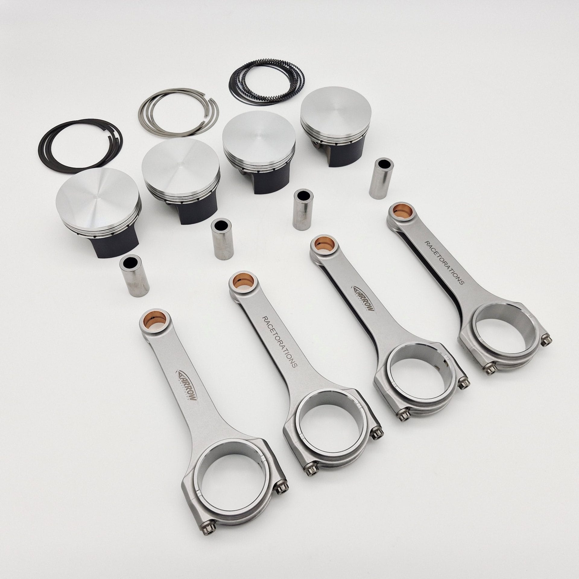The Racetorations 87mm Slipper Piston & Steel Connecting Rod Set for TR2-4A & Morgan +4 is shown on a white background, featuring four slipper pistons, four steel rods, piston pins, and rings—essential engine components.
